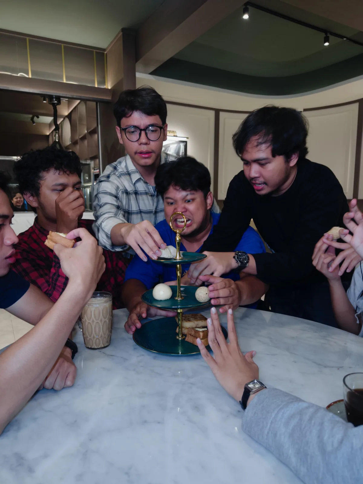 Friends reaching across a marble table for toast and dim sum on a tiered stand